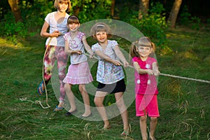 Group of happy children playing tug of war outside on grass