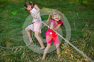 Group of happy children playing tug of war outside on grass