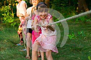 Group of happy children playing tug of war outside on grass