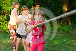 Group of happy children playing tug of war outside on grass