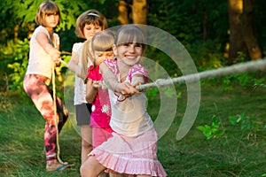 Group of happy children playing tug of war outside on grass