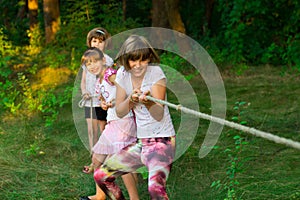 Group of happy children playing tug of war outside on grass