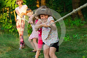 Group of happy children playing tug of war outside on grass