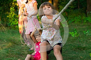 Group of happy children playing tug of war outside on grass