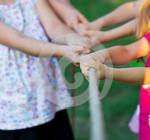 Group of happy children playing tug of war outside on grass. Kids pulling rope at park