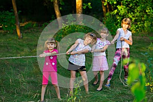 Group of happy children playing tug of war outside on grass. Kids pulling rope at park