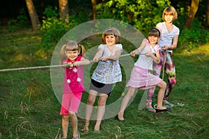 Group of happy children playing tug of war outside on grass. Kids pulling rope at park