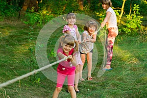 Group of happy children playing tug of war outside on grass. Kids pulling rope at park