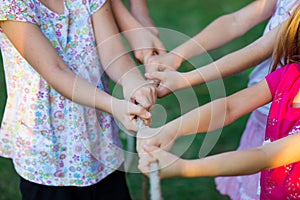 Group of happy children playing tug of war outside on grass. Kids pulling rope at park