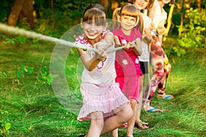 Group of happy children playing tug of war outside on grass. Kids pulling rope at park.