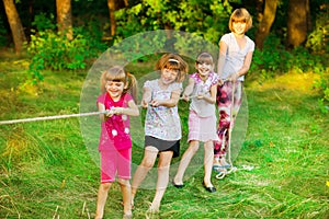 Group of happy children playing tug of war outside on grass. Kids pulling rope at park.