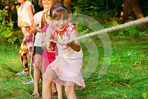 Group of happy children playing tug of war outside on grass. Kids pulling rope at park. Summer camp