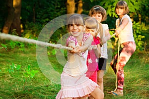 Group of happy children playing tug of war outside on grass. Kids pulling rope at park. Summer camp