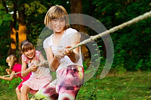 Group of happy children playing tug of war outside on grass. Kids pulling rope at park. Summer camp