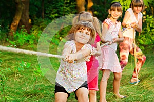 Group of happy children playing tug of war outside on grass. Kids pulling rope at park. Summer camp