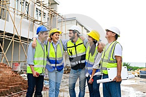 Group of happy contractors, engineers and formats in safety vests with helmets stand on the under-construction building site.