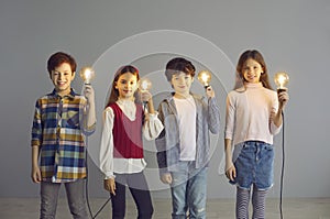 Group of happy creative children standing in studio and holding shining light bulbs