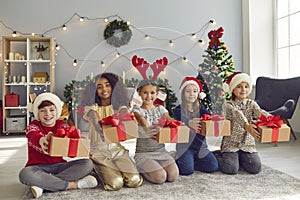 Group of happy diverse children sitting on the floor and holding Christmas presents