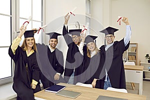 Group of happy diverse college or university graduates holding up diplomas and smiling