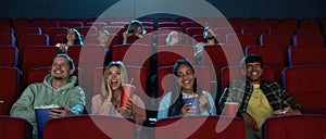 A group of happy diverse friends laughing while watching movie together, sitting in cinema auditorium