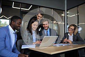 Group of happy diverse male and female business people in formal gathered around laptop computer in bright office.