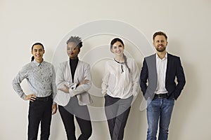 Group of happy diverse people in office wear standing near wall and smiling at camera