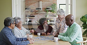 Group of happy diverse senior friends drinking coffee and doing puzzle at home