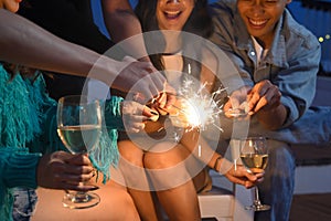 Group of happy friends celebrating at rooftop with sparklers. Holiday celebration, festive and friendship concept