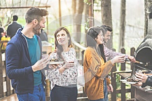 Group of happy friends cooking and eating at barbecue dinner outdoor - Young people toasting wine for bbq in wood house backyard