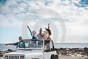 Group of happy friends doing excursion on desert in convertible 4x4 car - Young people having fun traveling together - Friendship