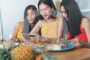 Group of happy friends eating dinner together and shel taking photo of food on the table