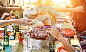 Group of happy friends eating and drinking beers at barbecue dinner at sunset - Adult people having meal together outdoor - Focus