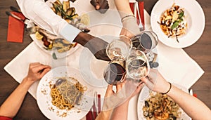 Group of happy friends eating and drinking pasta, pizza and wine - people having meal in restaurant - Focus on wine glasses -