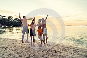 Group of happy friends enjoying beautiful sunset at the tropical beach, jumping and having fun together. Travelers