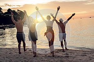 Group of happy friends enjoying beautiful sunset at the tropical beach, jumping and having fun together. Travelers