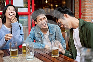 Group of happy friends are enjoying talking and drinking beers while hanging out at a restaurant