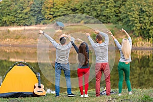 Group of happy friends with guitar, having fun outdoor, dancing hold hands up  near the lake in the park background the Beautiful