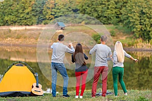 Group of happy friends with guitar, having fun outdoor, dancing hold hands up  near the lake in the park background the Beautiful