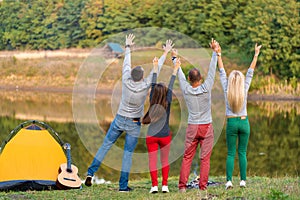 Group of happy friends with guitar, having fun outdoor, dancing hold hands up  near the lake in the park background the Beautiful