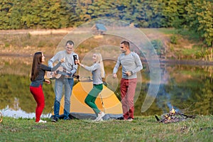 Group of happy friends with guitar, having fun outdoor, dancing and jumping near the lake in the park background the Beautiful sky