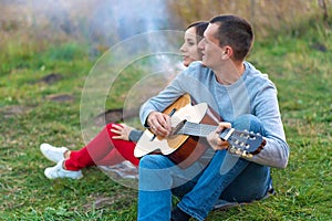 Group of happy friends with guitar, having fun outdoor, near bonfire and tourist tent. Camping fun happy family