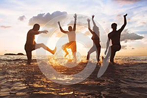 Group of happy friends or family having fun together on the beach at sunset, jumping and dancing