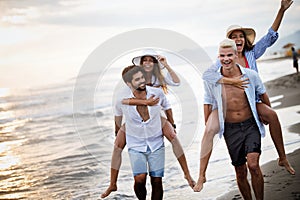 Group of happy friends having fun walking down the beach at sunset