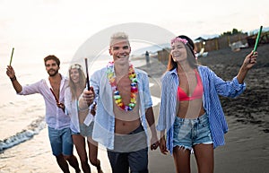 Group of happy friends having fun walking down the beach at sunset