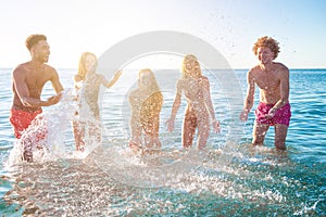 Group of happy friends having fun with water sea at ocean beach at dawn