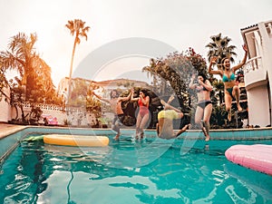 Group of happy friends jumping in pool at sunset time - Crazy young people having fun making party in exclusive tropical house