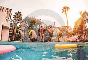 Group of happy friends jumping in pool at sunset time - Millennial young people having fun making party in exclusive resort