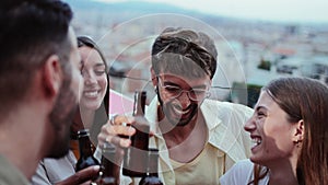 Group of happy friends laughing and having fun celebrating a evening late rooftop party, toasting beer bottles