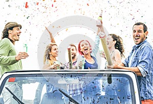 Group of happy friends making party throwing confetti on convertible jeep car