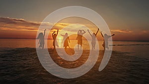 Group of happy friends running in to water at sunset - Silhouettes of active people having fun on the beach on vacation